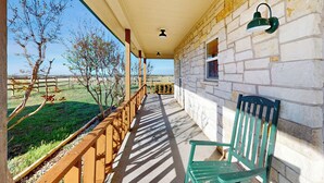 Un portico riparato con ringhiera in legno, una sedia verde e un muro di pietra con una finestra.