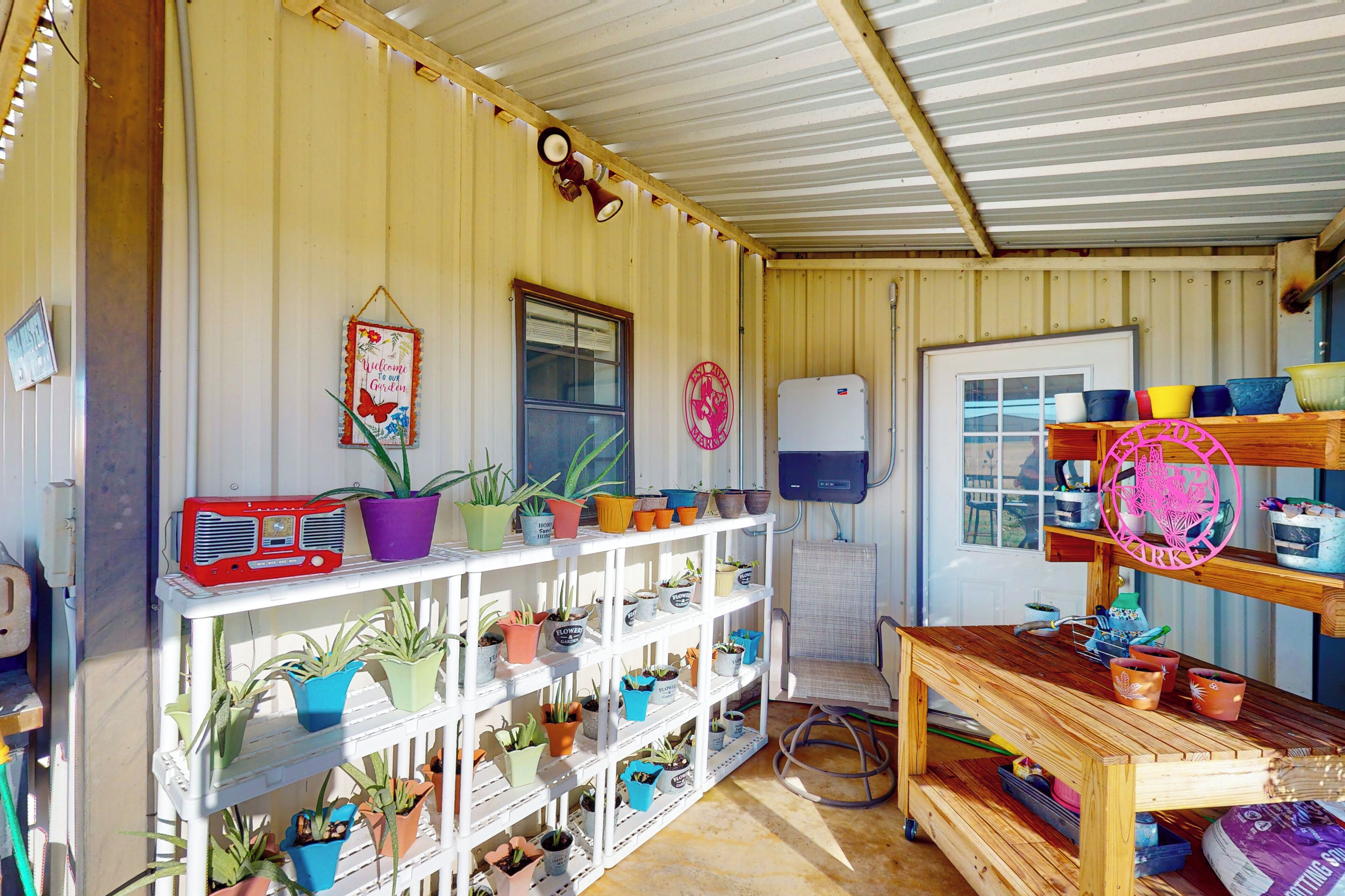 Een rustiek interieur met een houten tafel, planken met potplanten, een vintage radio en een deur met een ronde decoratie.