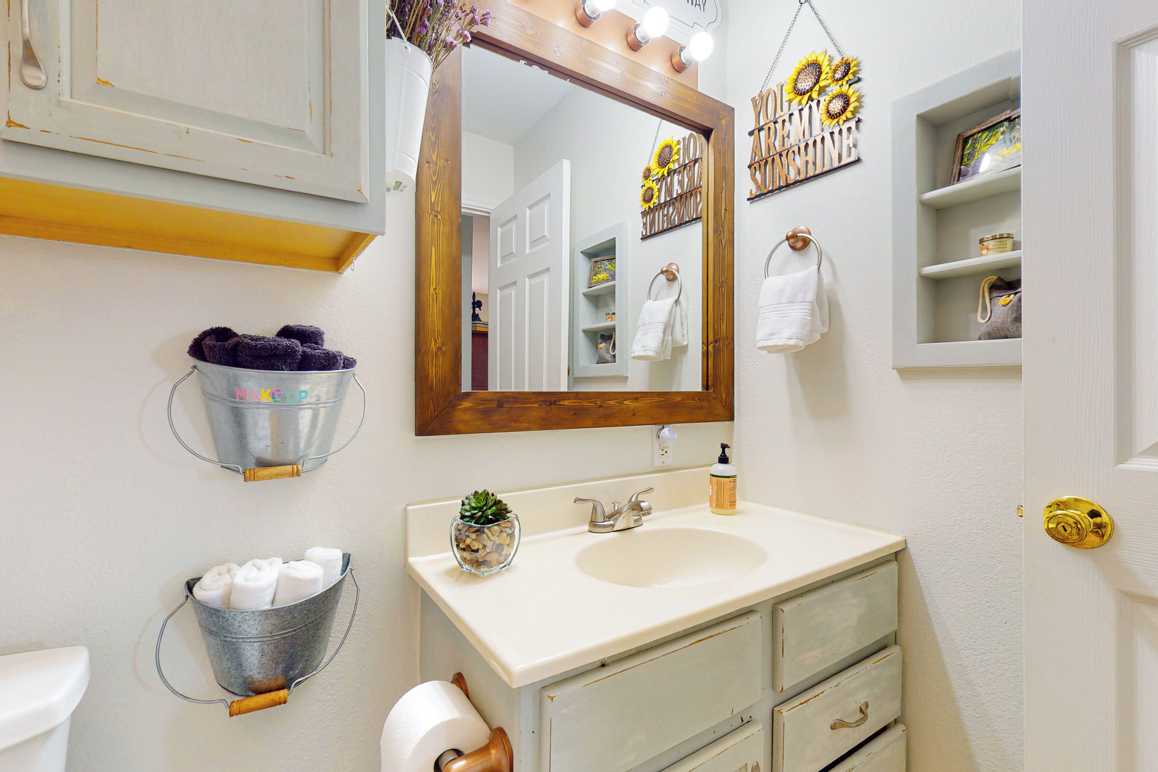 A bathroom with a white sink, a mirror, a towel rack, and a shelf with toiletries.