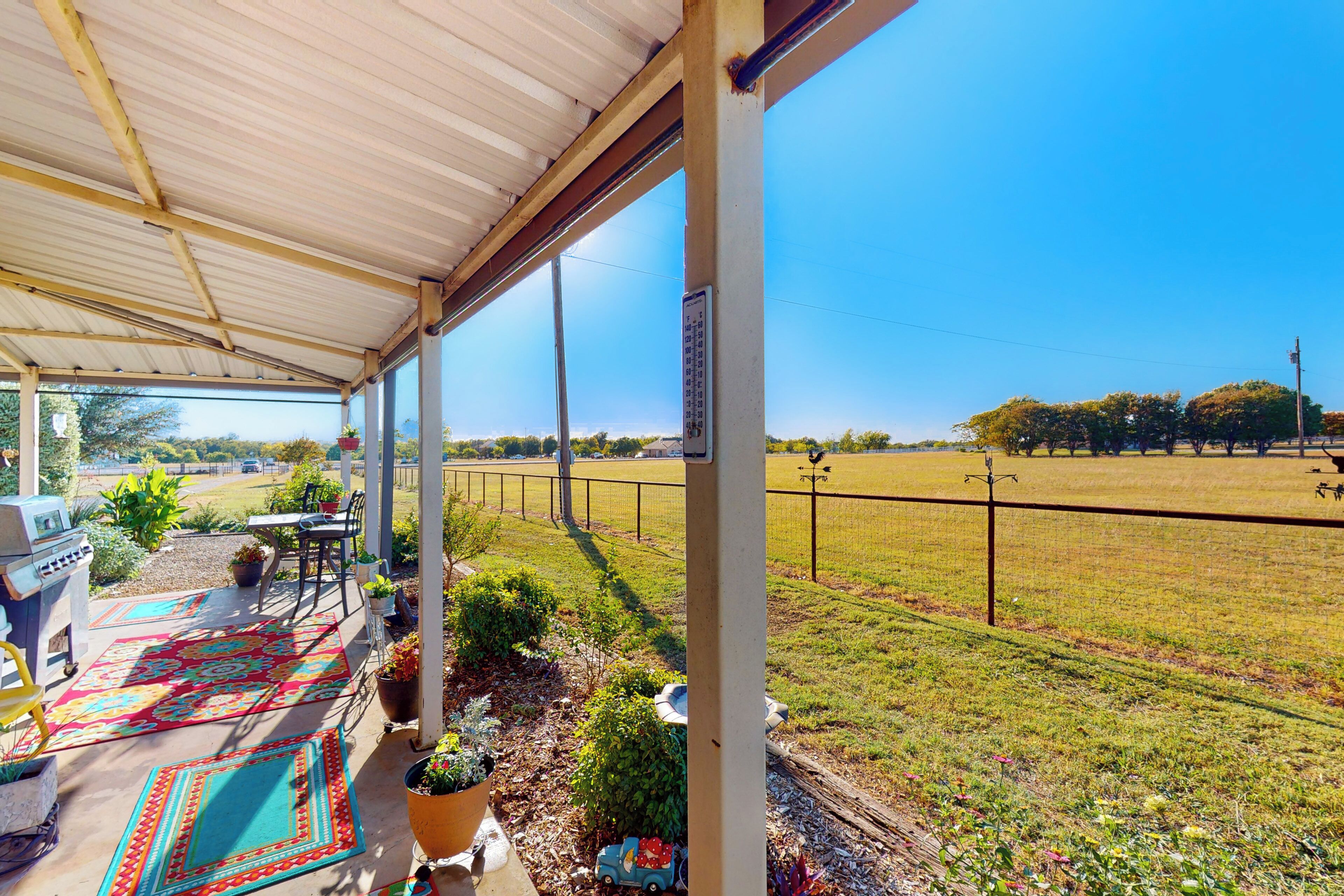 A covered patio with a grill, outdoor seating, and a view of a grassy field.