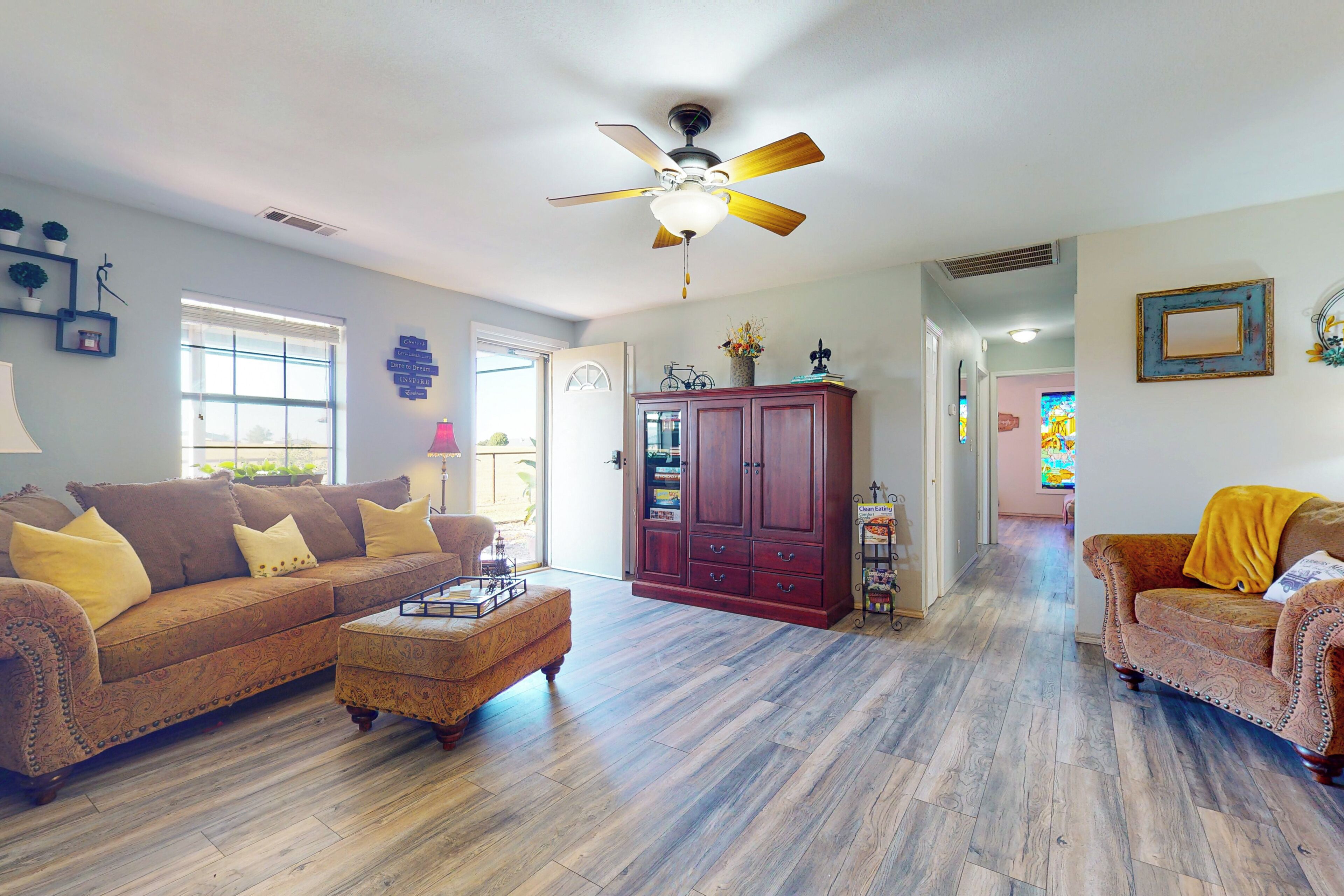 A spacious living room with hardwood flooring, a ceiling fan, a wooden cabinet, and a sofa.