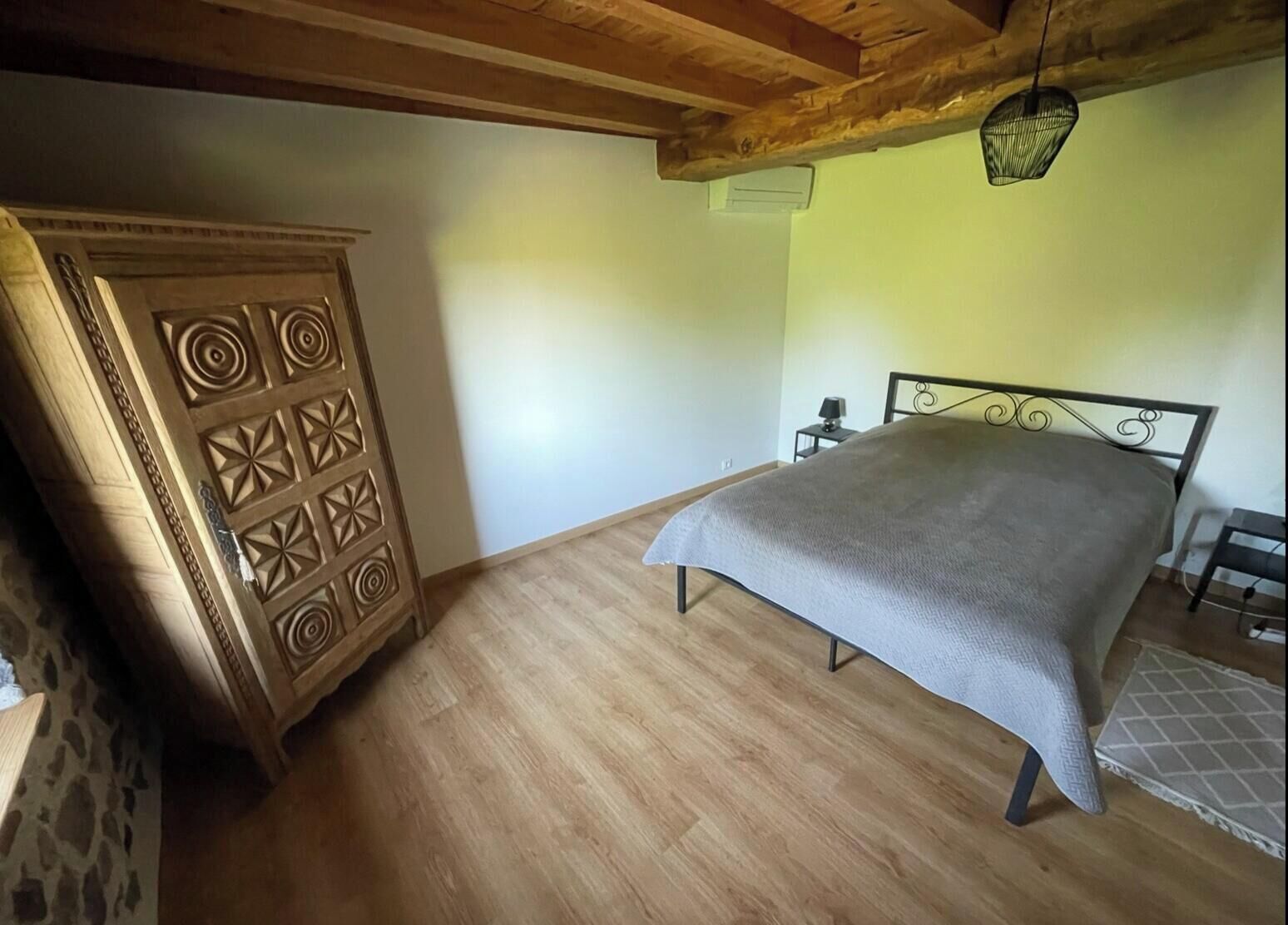 A bedroom with a bed, a wooden wardrobe, and a hanging light fixture.