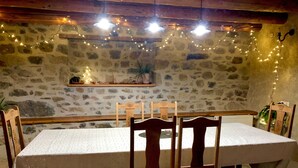Un comedor con paredes de piedra, una mesa cubierta con mantel blanco, sillas de madera y luces colgantes.