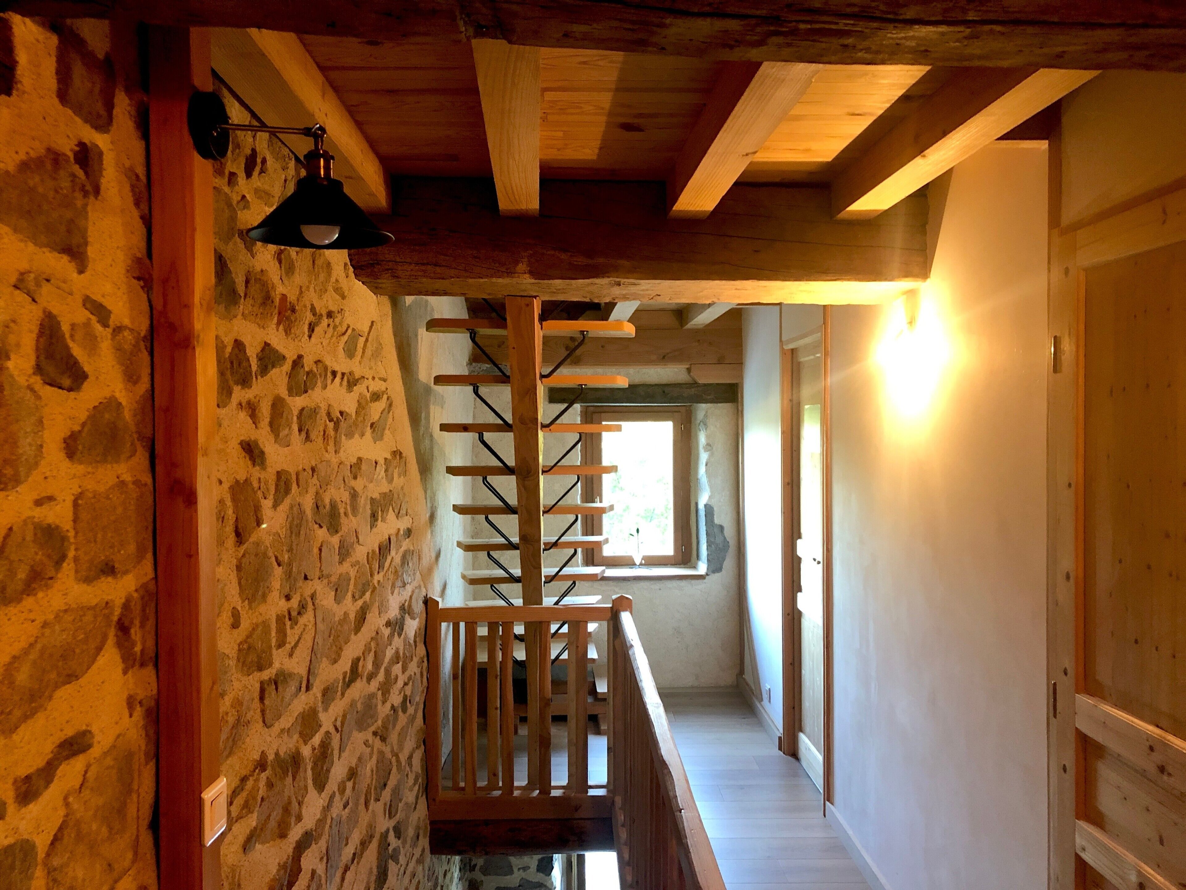 A stone wall, wooden beams, a staircase, and a window with natural light.