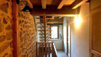 Pared de piedra, vigas de madera, una escalera y una ventana con luz natural.