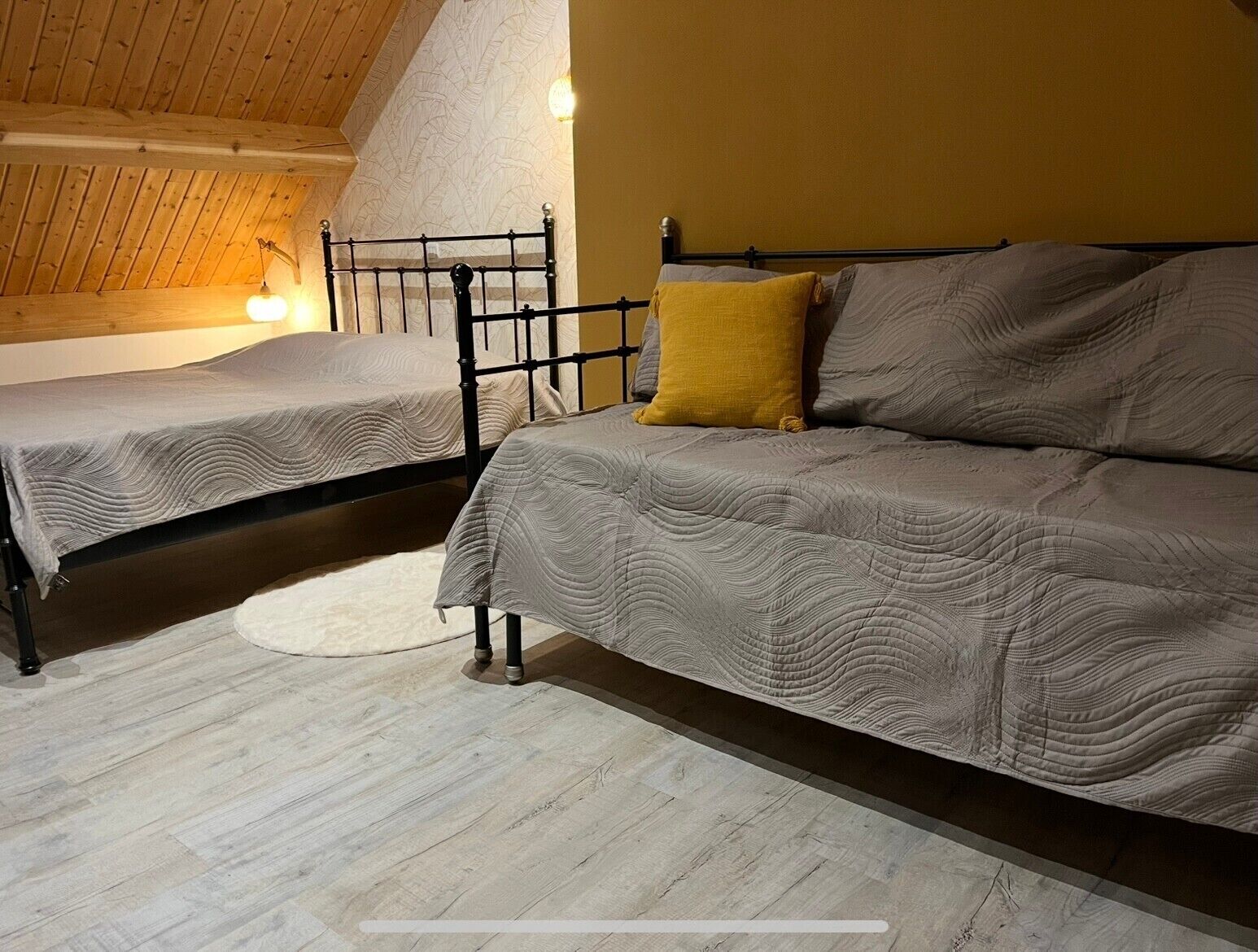 A room with two beds, a wooden ceiling, and a white rug.