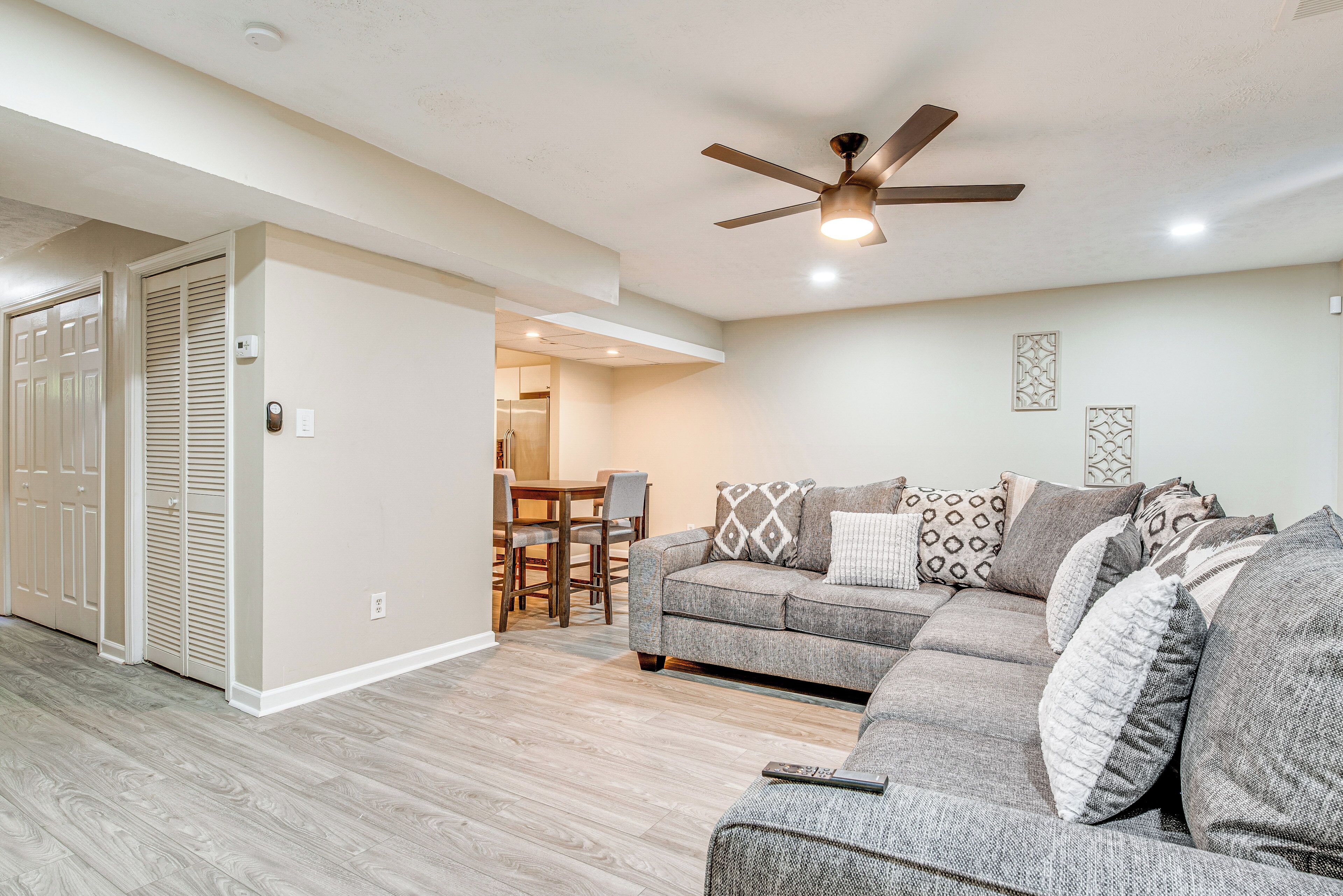 A living room with a gray sofa, patterned cushions, a ceiling fan, and a dining area in the background.