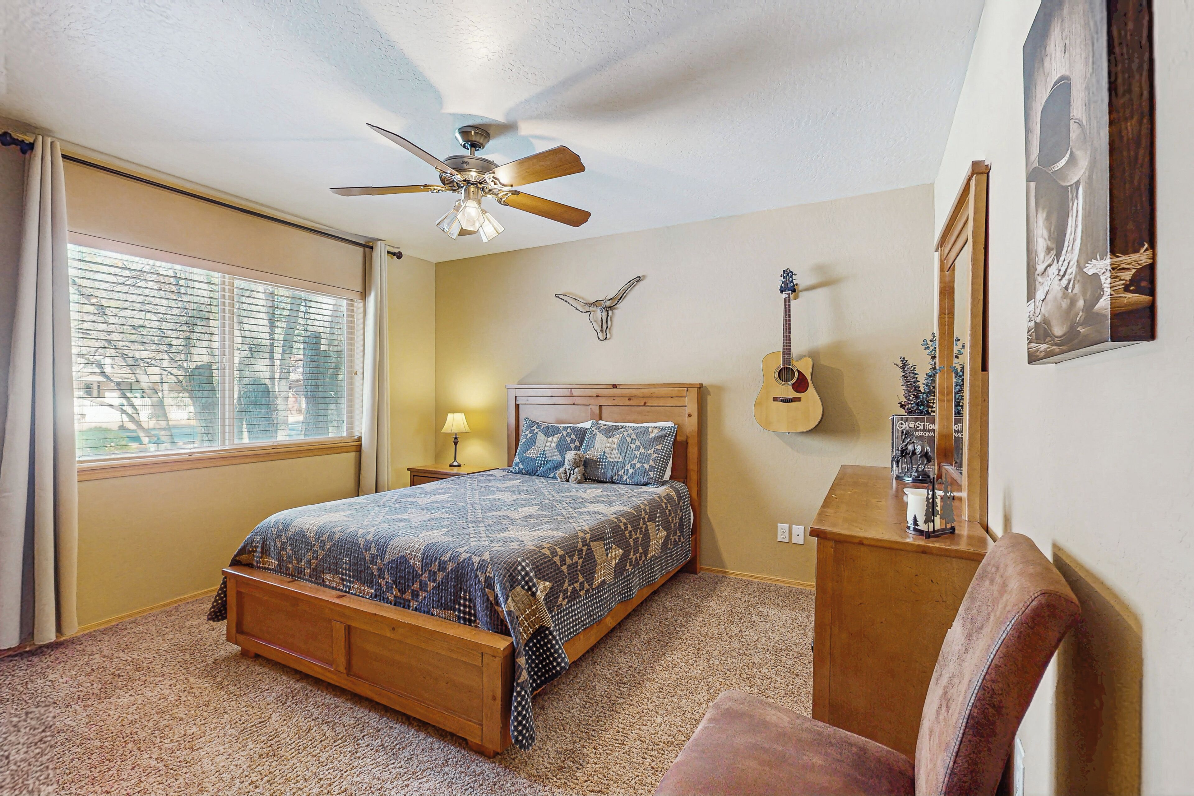 A bedroom with a wooden bed, a ceiling fan, a guitar, and a wall-mounted mirror.