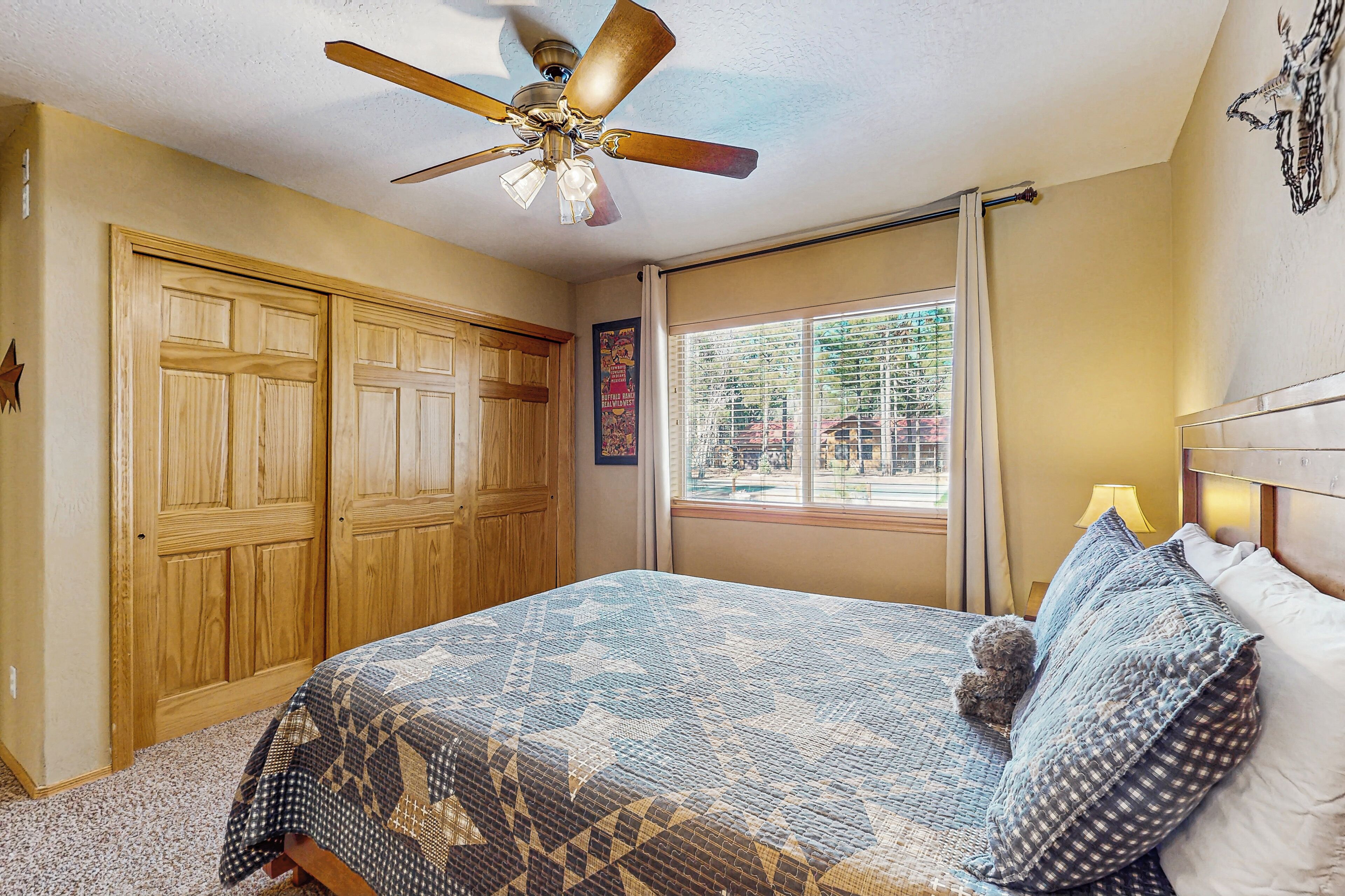 A bedroom with a bed, a ceiling fan, wooden wardrobes, a window with blinds, and a wall-mounted lamp.