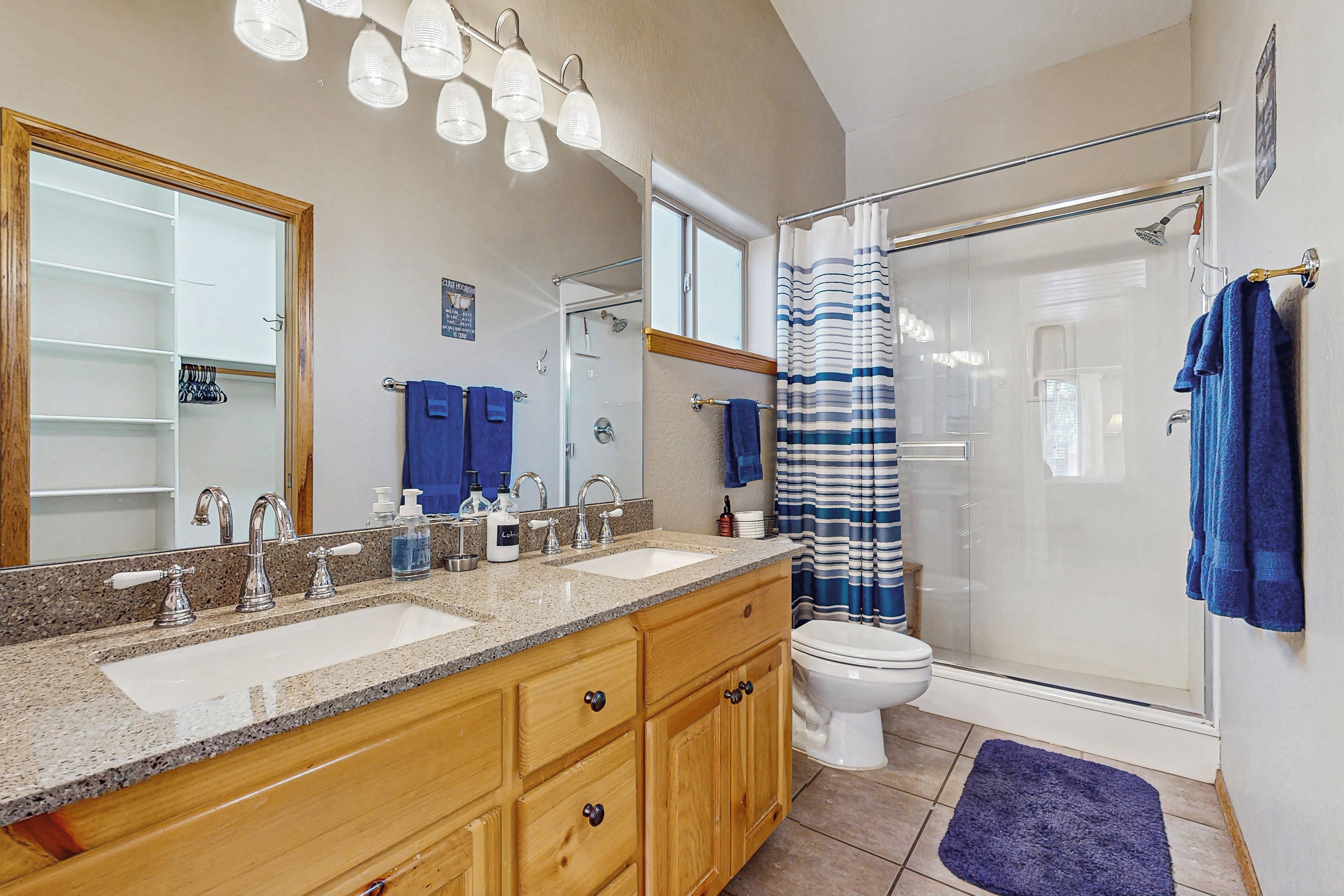 A bathroom with a double sink vanity, a toilet, a glass shower enclosure, and a blue shower curtain.