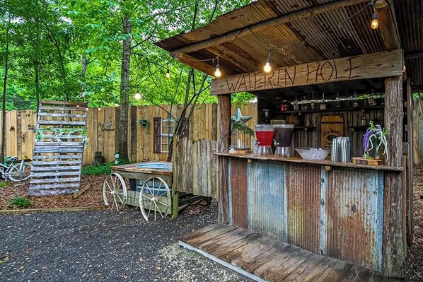 Eine rustikale Bar im Freien namens "WATERMAN HOLI" mit Holzbalkon, einer Bar und einem Fahrrad im Hintergrund.
