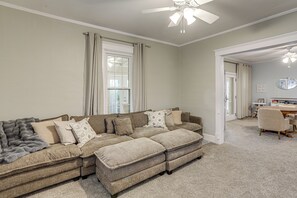 Ein Wohnzimmer mit Ecksofa, Deckenventilator und Blick in einen anderen Raum.