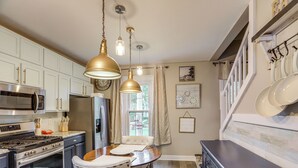A kitchen with white cabinets, stainless steel appliances, and a dining area with a white table and chairs. - 2 Mi to Dtwn: Charming Sandusky Getaway w/ Hot Tub (Sandusky)
