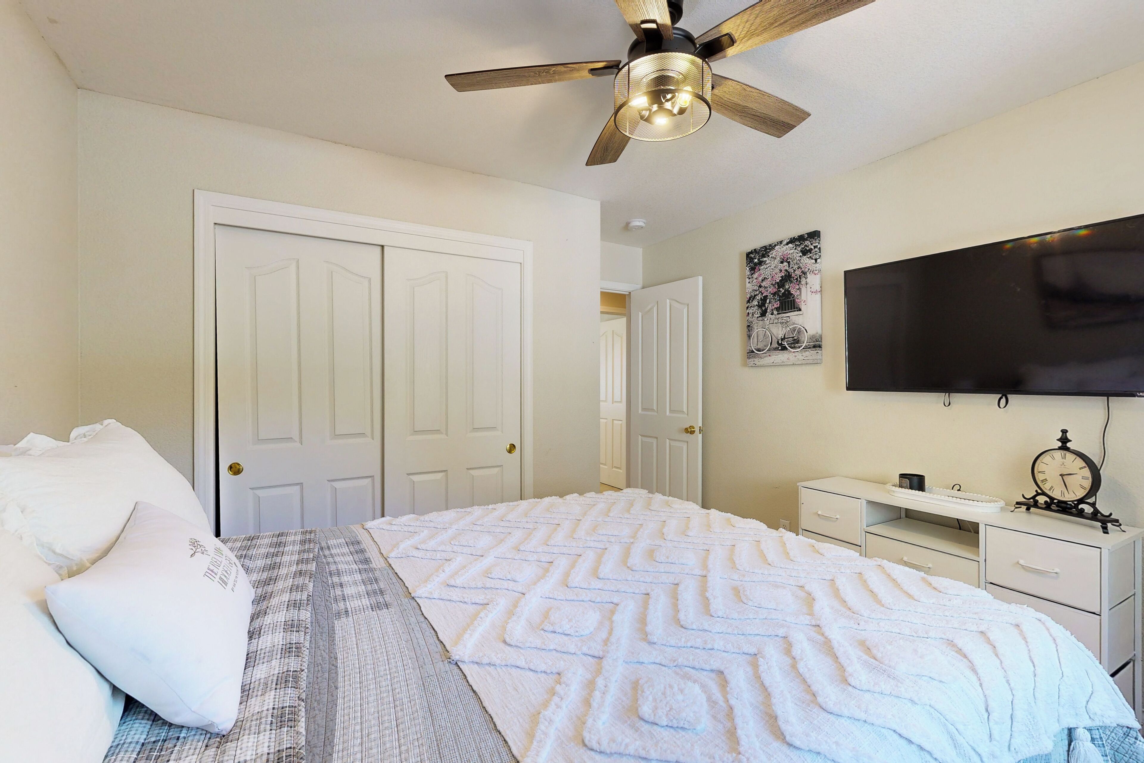 A bedroom with a bed, a ceiling fan, a TV, and a desk with drawers.