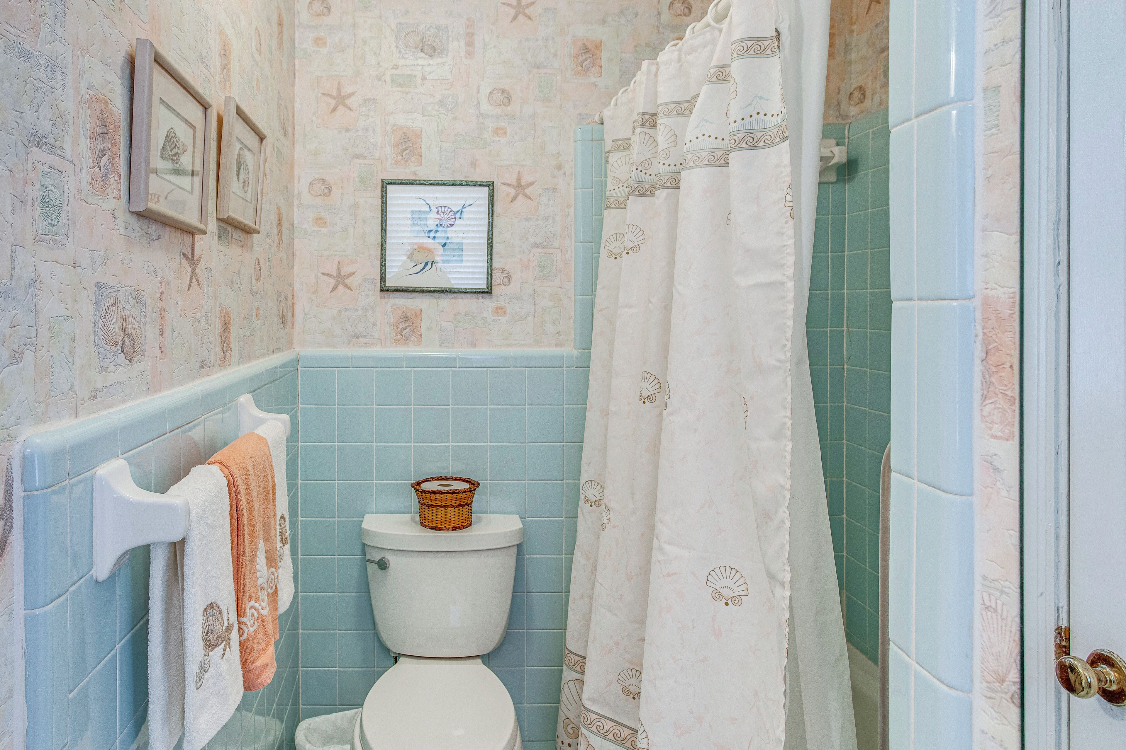 Ein Badezimmer mit Toilette, einem Handtuchhalter mit Handtüchern, einem gerahmten Bild an der Wand und einer Duschvorhang.