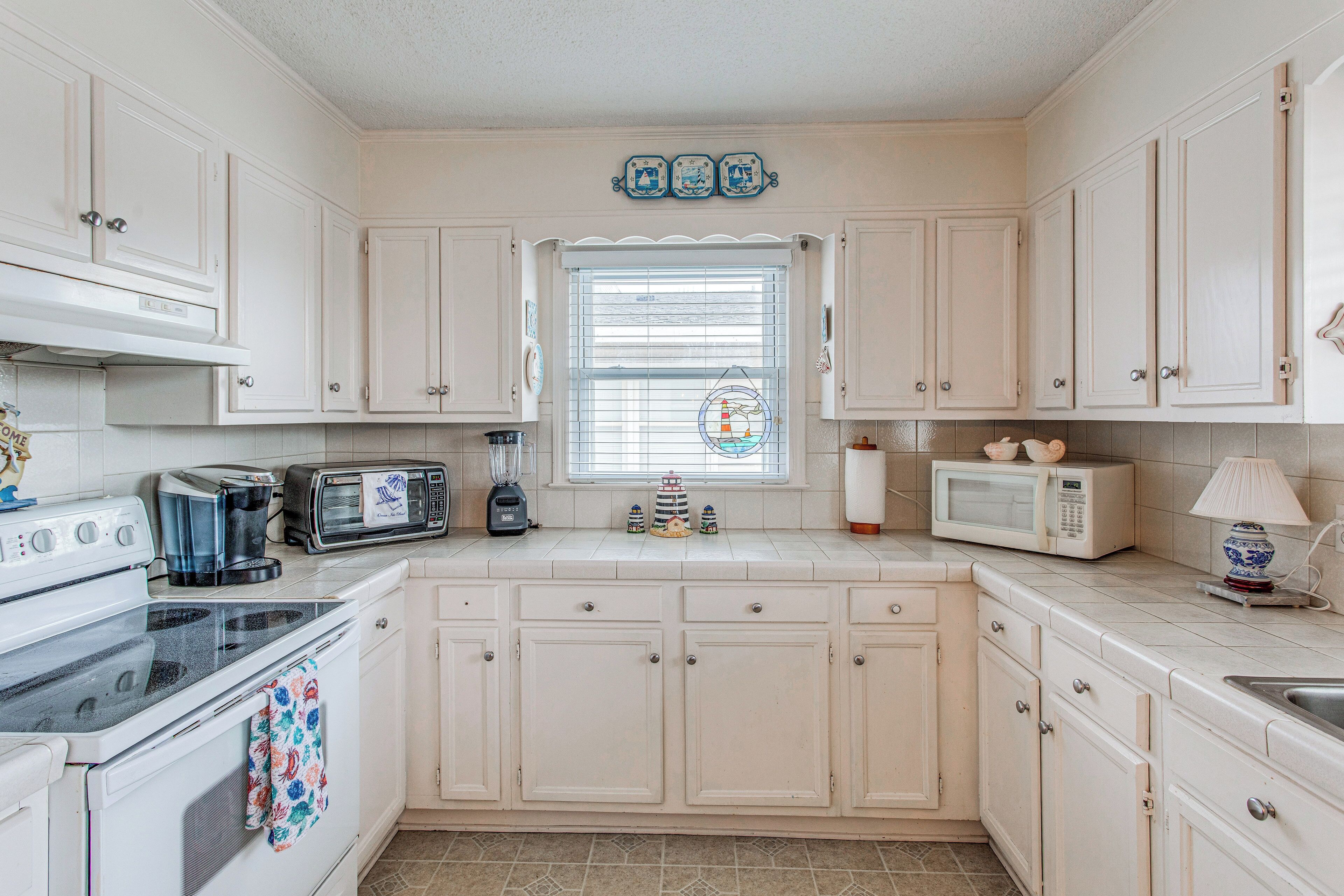 A kitchen with white cabinets, a stove, a microwave, a toaster, and a window with blinds.