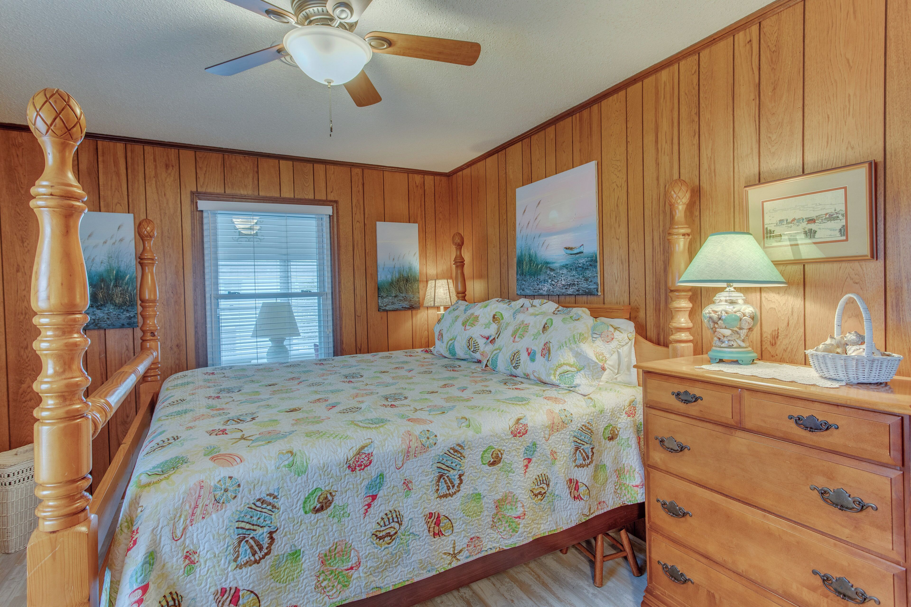 A bedroom with a wooden paneled wall, a four-poster bed, a ceiling fan, and a dresser with drawers.