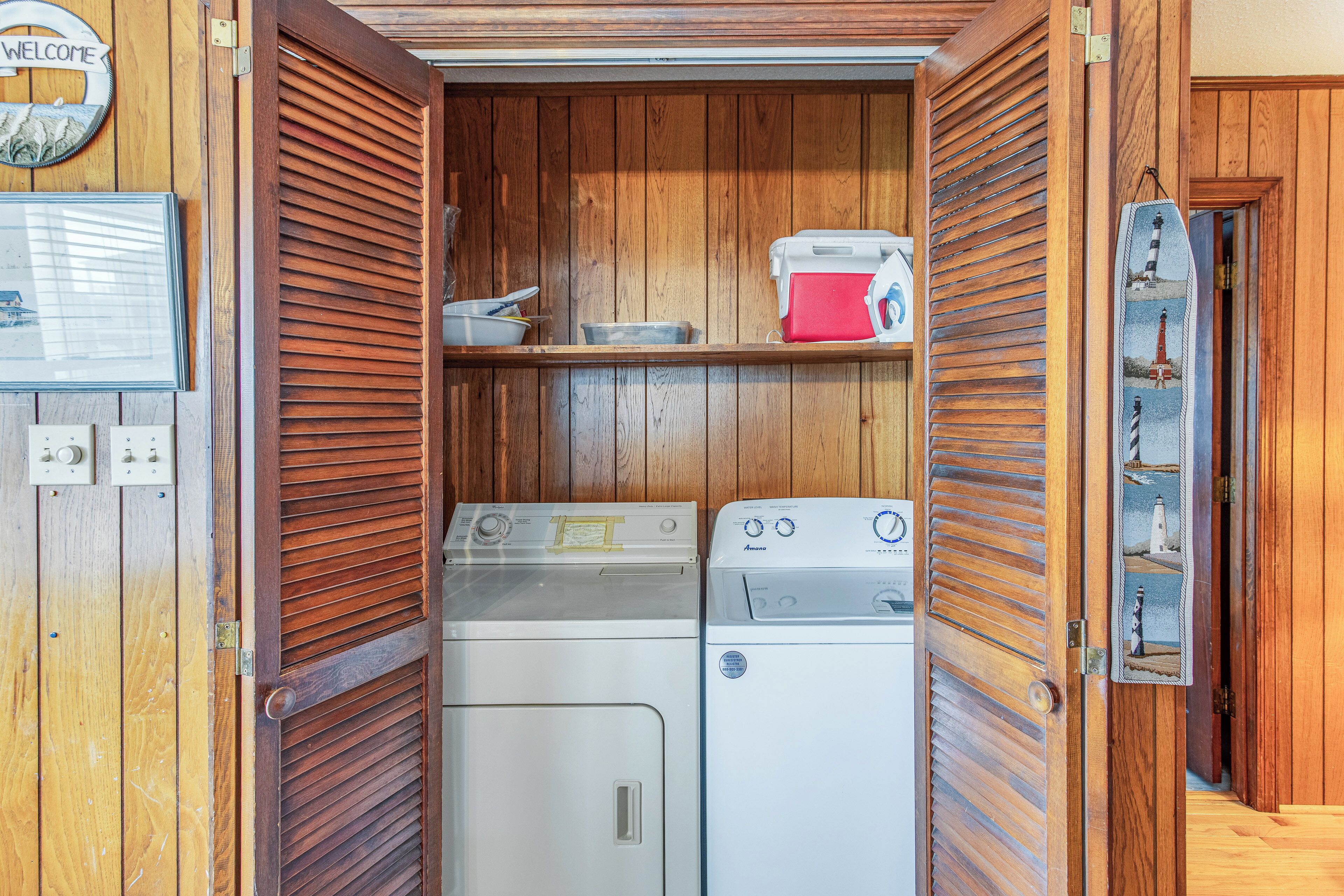 A laundry room with wooden paneling, two washing machines, a red cooler, and a welcome sign.