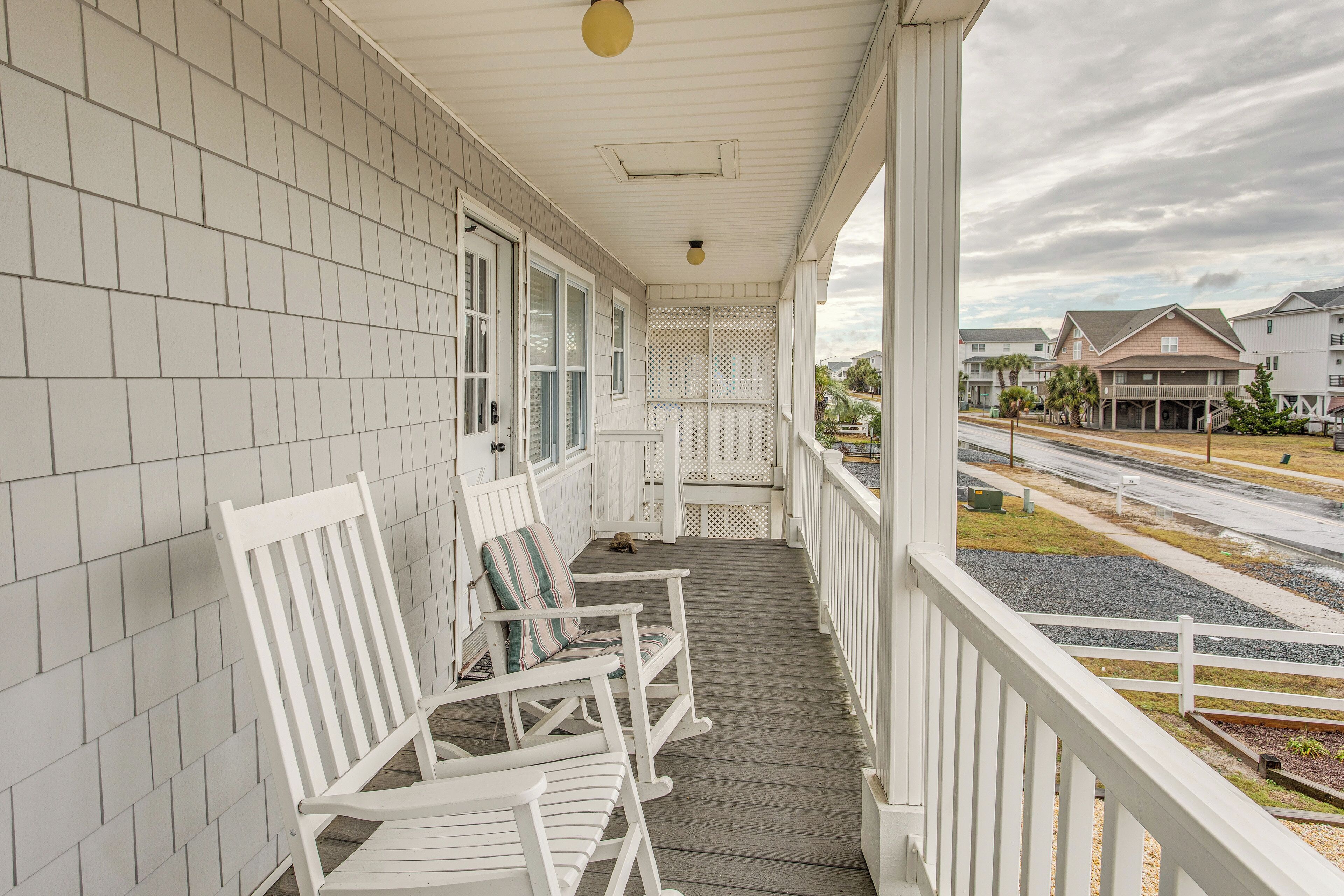 A covered porch with white railings and a view of a residential street.