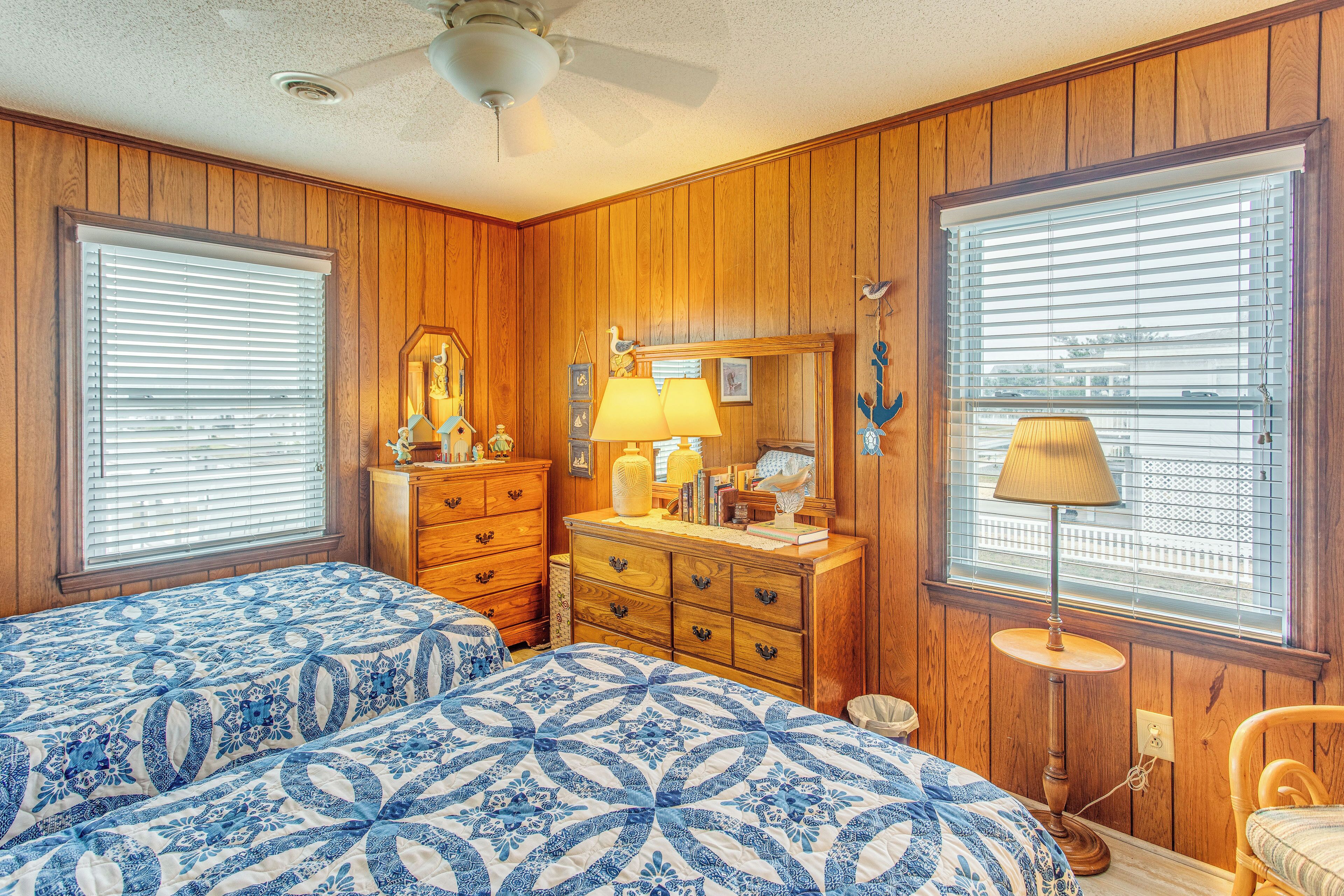 A room with two beds, wooden walls, a dresser, a mirror, and a window with blinds.