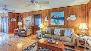 A living room with wooden paneling, a beige sofa, two armchairs, a coffee table, and a ceiling fan. - Steps to Sand! Family Ocean Isle Beach Retreat (Ocean Isle Beach)