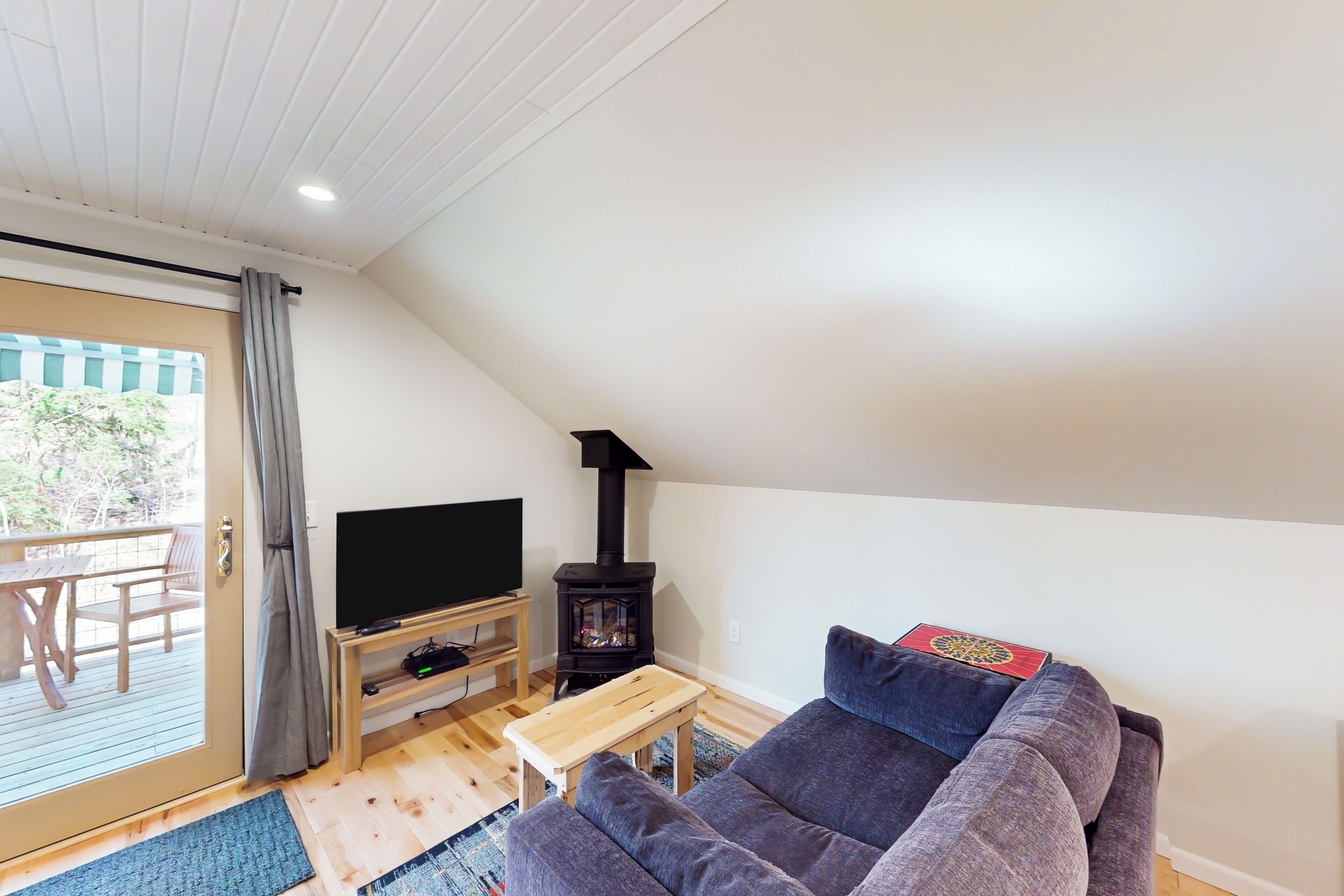 Un salon comprenant un canapé, un téléviseur, une table en bois, une cheminée et une vue sur l’extérieur, visible à travers une porte vitrée.