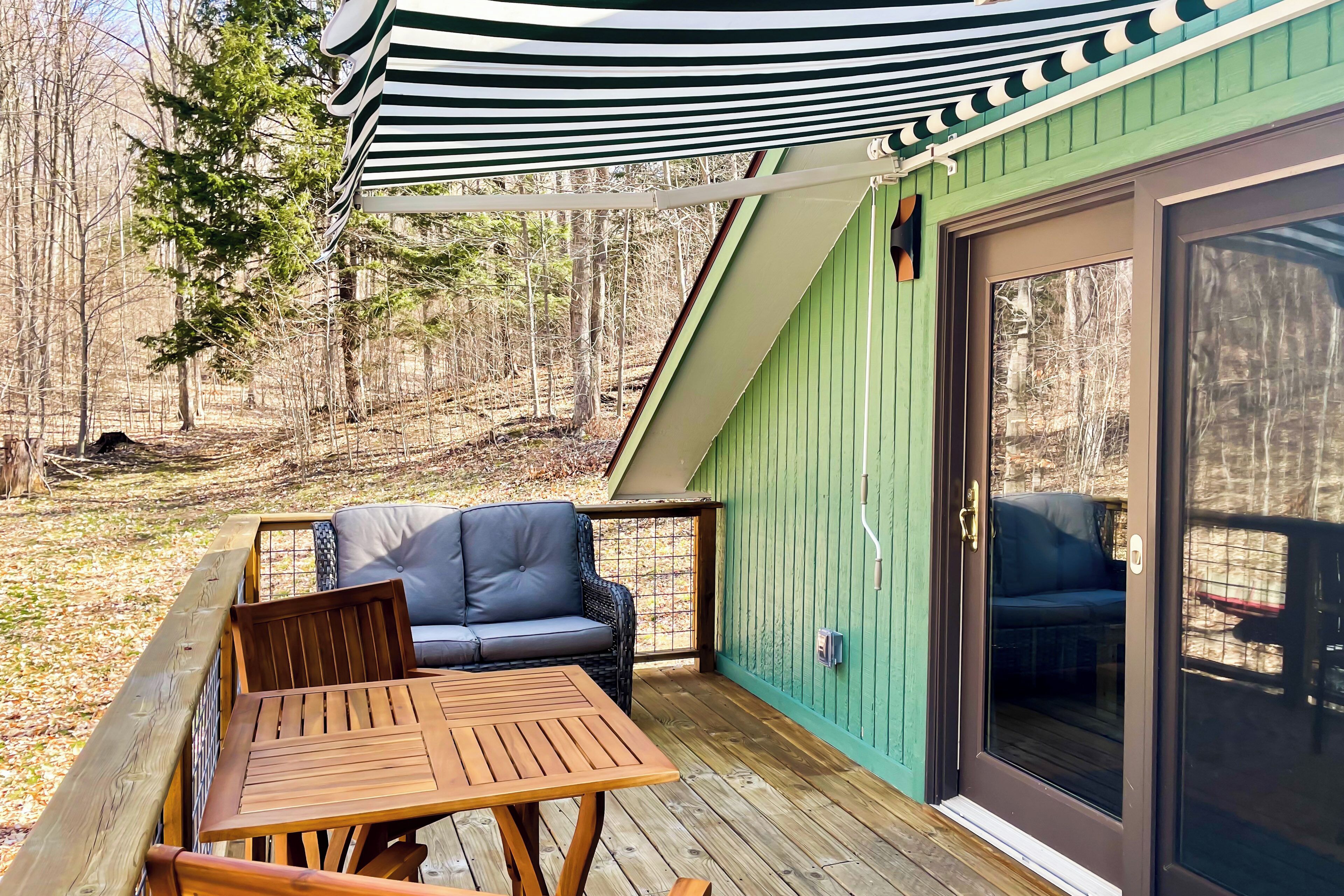 Una terraza de madera con una mesa y sillas, una pared verde y un ventanal corredero.