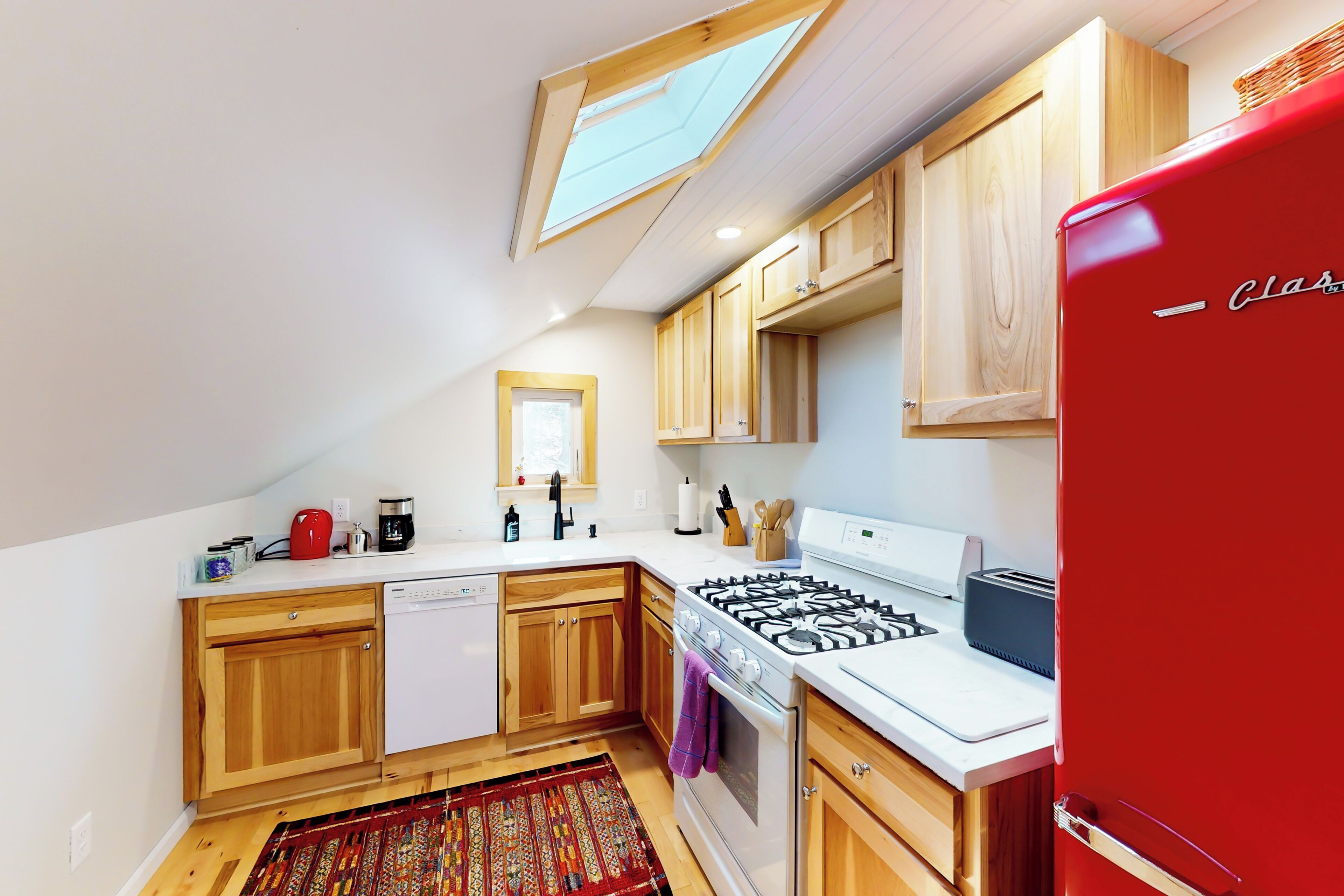 A kitchen with wooden cabinets, a red refrigerator, a gas stove, and a skylight.