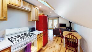 A compact kitchen with a gas stove, a red refrigerator, wooden cabinets, and a dining area with a chair and table. - Half-mile to Crystal Lake! Couples Retreat w/ Deck (Beulah)