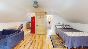 A loft bedroom with a wooden floor, a sofa, a bed with a patterned bedspread, a red cabinet, and a skylight. - Half-mile to Crystal Lake! Couples Retreat w/ Deck (Beulah)