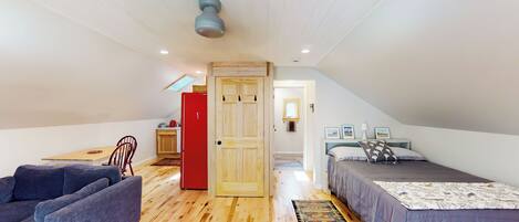 Un dormitorio tipo loft con piso de madera, un sofá, una cama con colcha estampada, un armario rojo y un tragaluz.