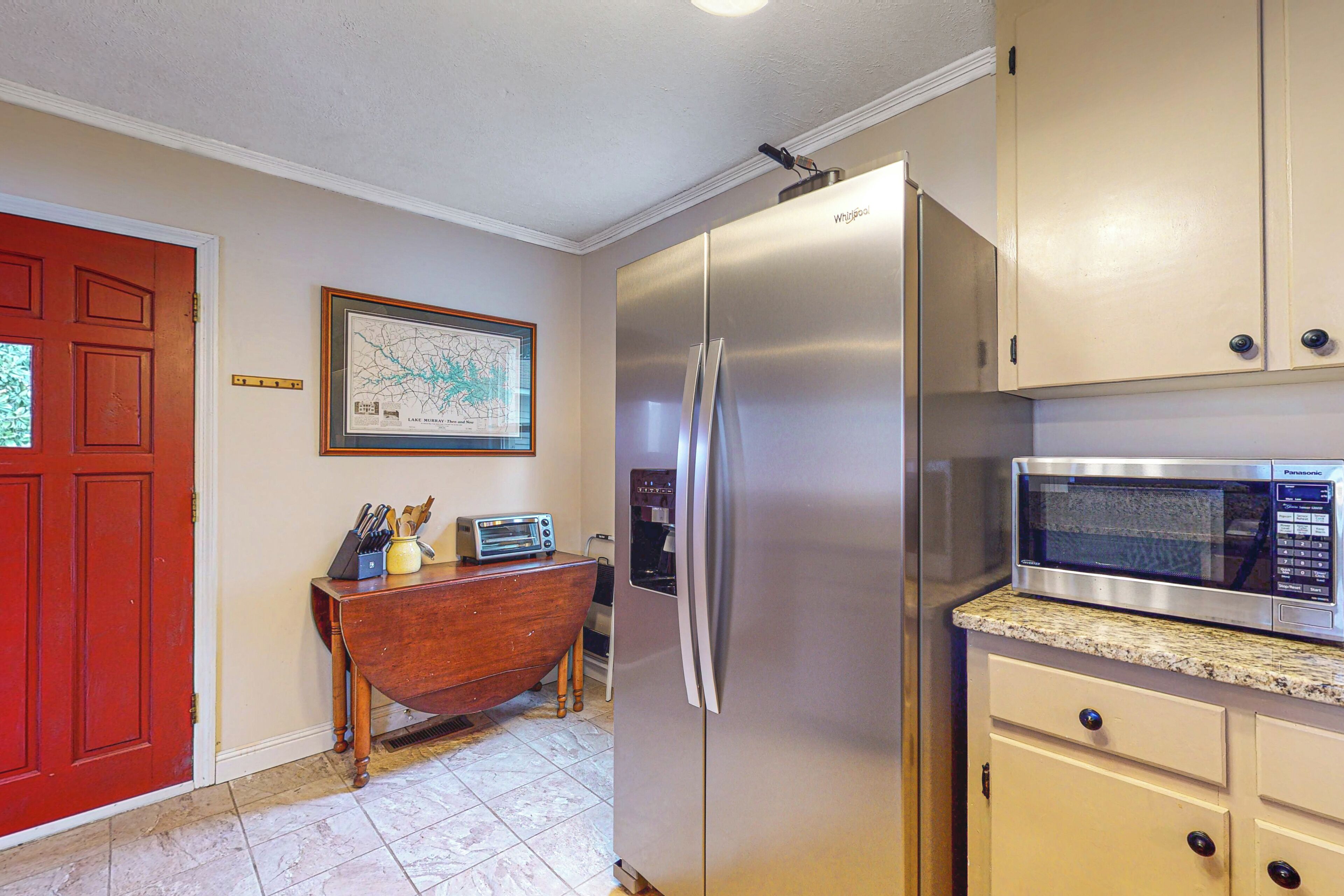 A kitchen with a stainless steel refrigerator, a microwave, and a wooden table with kitchen utensils.