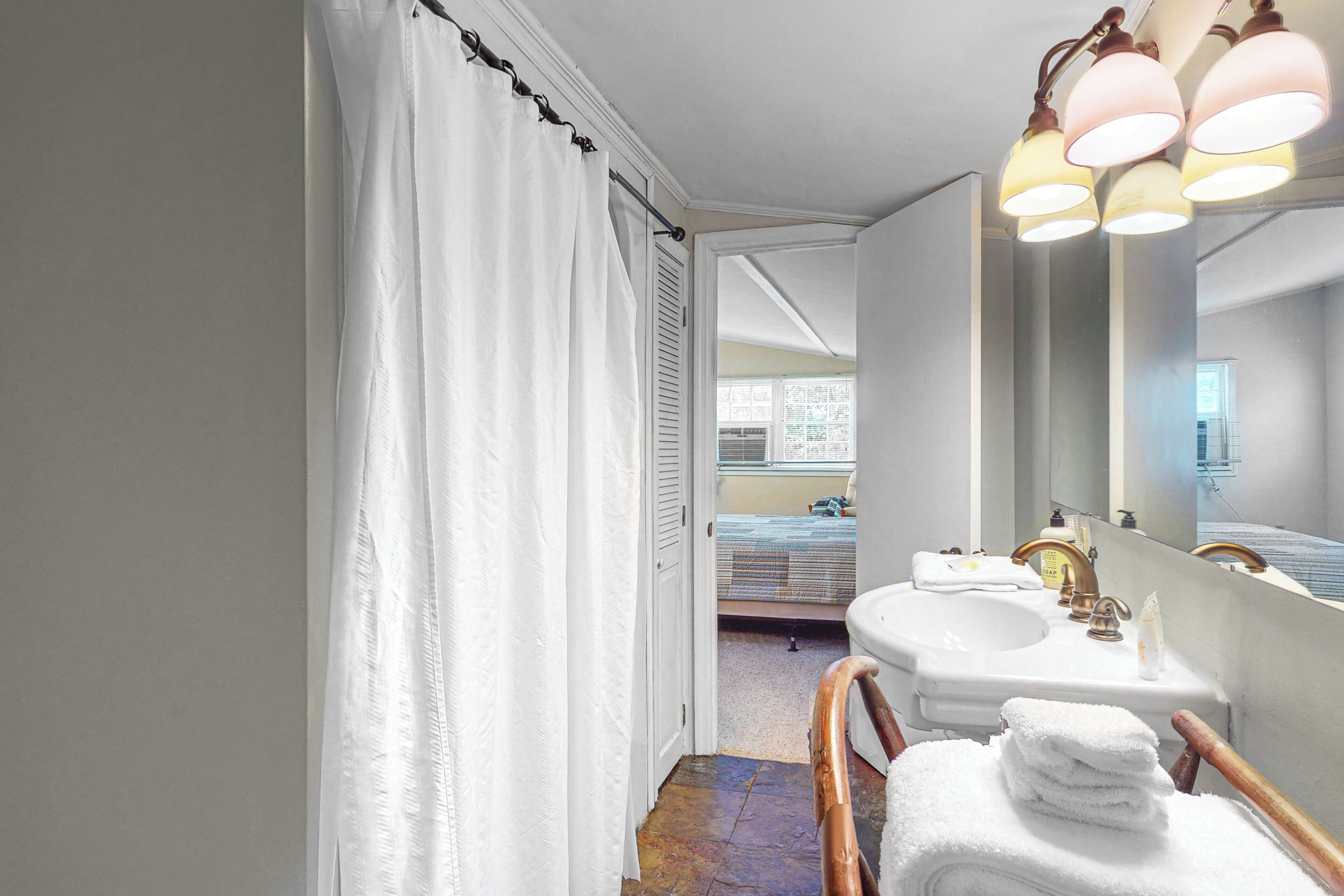 Un baño con cortina de ducha, un lavamanos con espejo y una silla de madera.