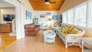 A spacious living room with a ceiling fan, a brown leather sofa, a white wicker sofa, a glass coffee table, and artwork on the walls. - 3BR Lakefront Lake Murray w/ Dock, Dog Friendly (Leesville)