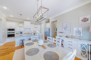 A modern kitchen with white cabinetry, a central island with stools, and pendant lighting. - 3BR Home Near Beach w/ Views, Deck & Grill (Gulfport)