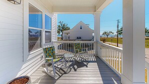 A wooden porch with white railings, two rocking chairs with patterned cushions, and a potted plant. - 3BR Home Near Beach w/ Views, Deck & Grill (Gulfport)