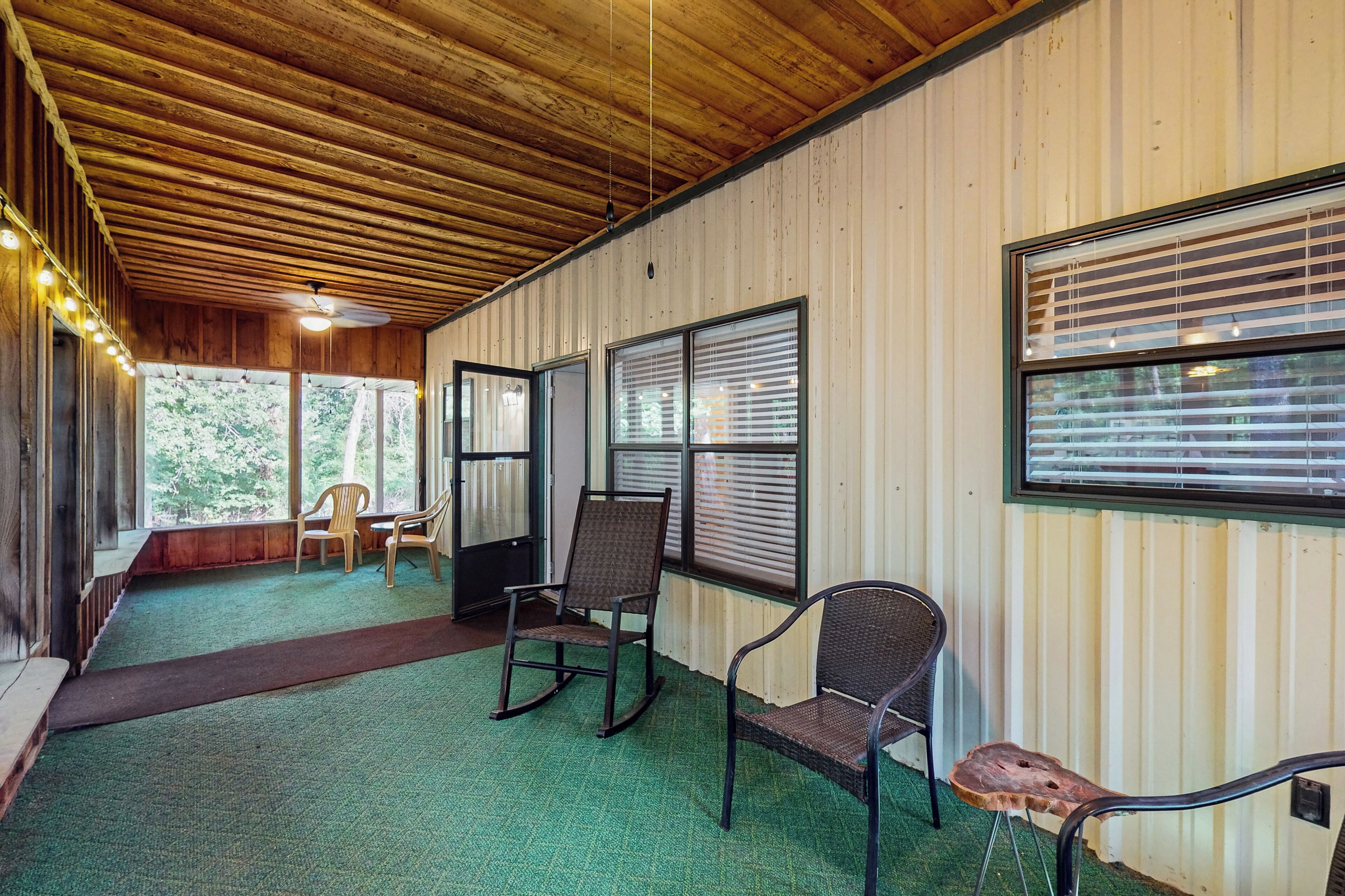 Une véranda couverte avec un plafond en bois, une moquette verte et plusieurs chaises.
