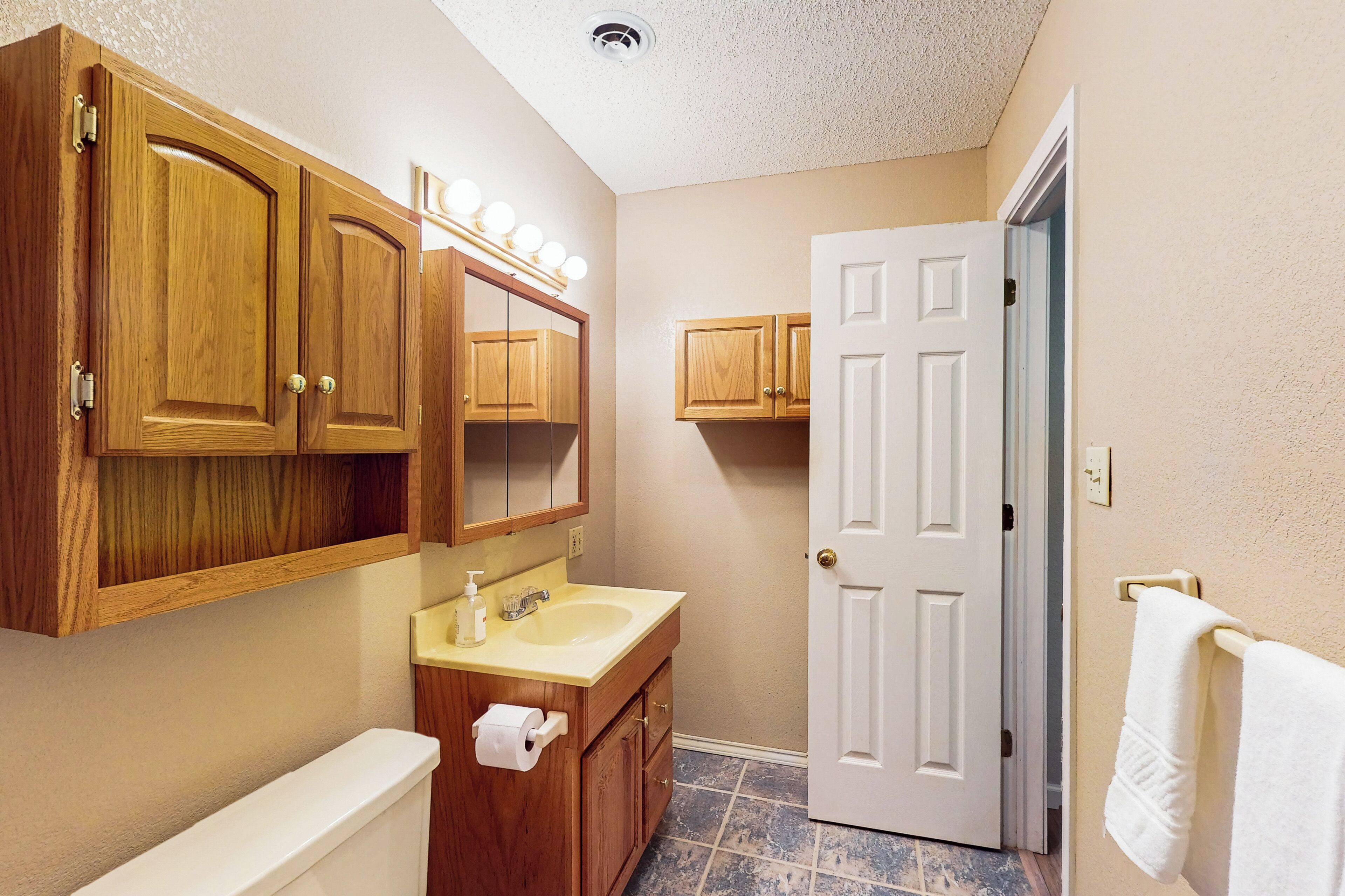 A bathroom with wooden cabinets, a sink, a toilet, and a white door.