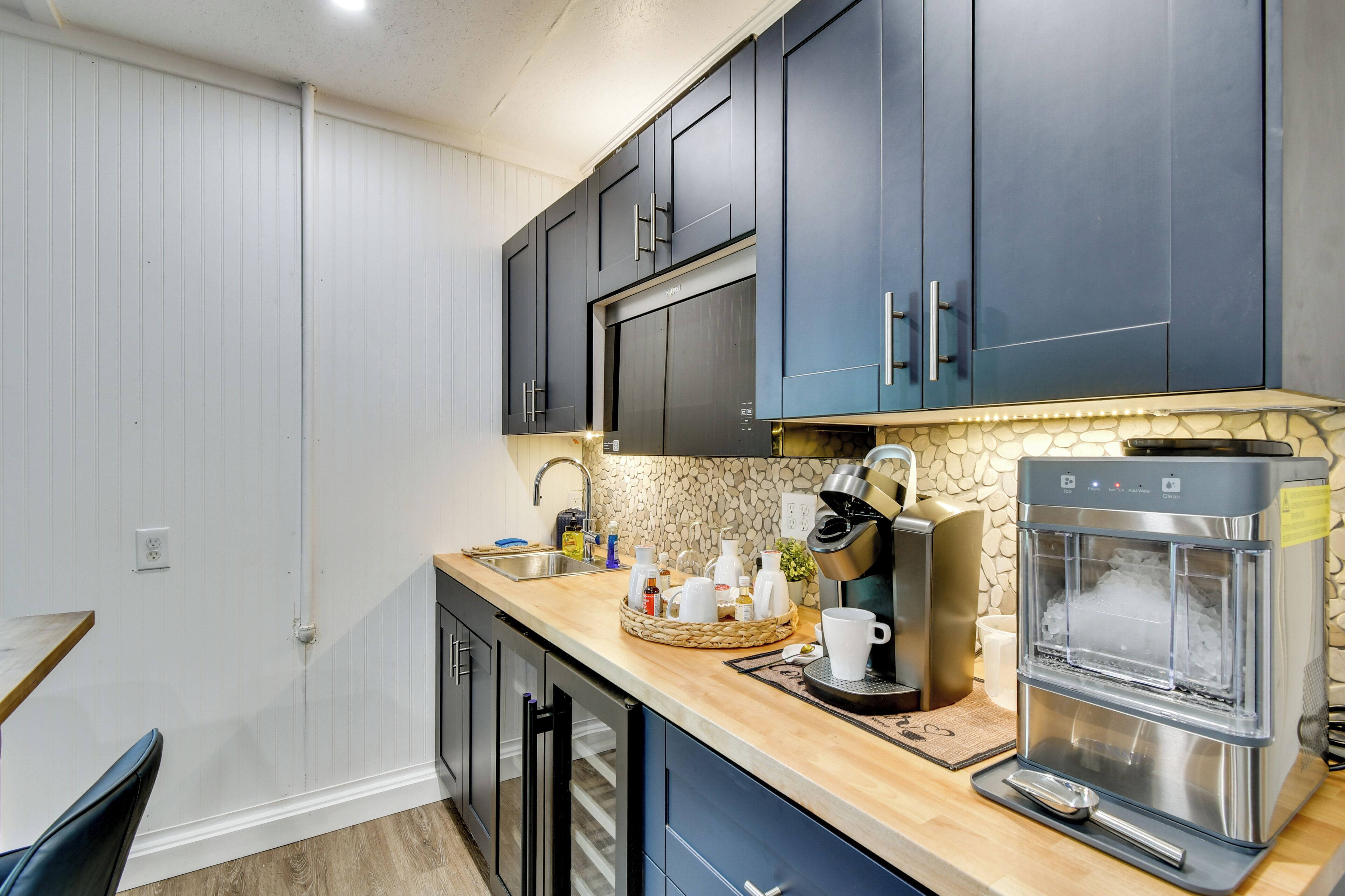 A modern kitchen with dark blue cabinets, a stone backsplash, a coffee machine, and a water dispenser.