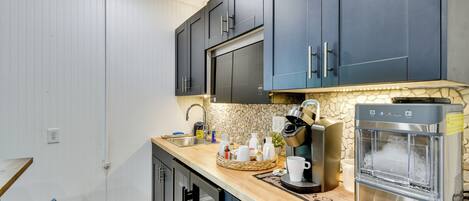 A modern kitchen with dark blue cabinets, a stone backsplash, a coffee machine, and a water dispenser.