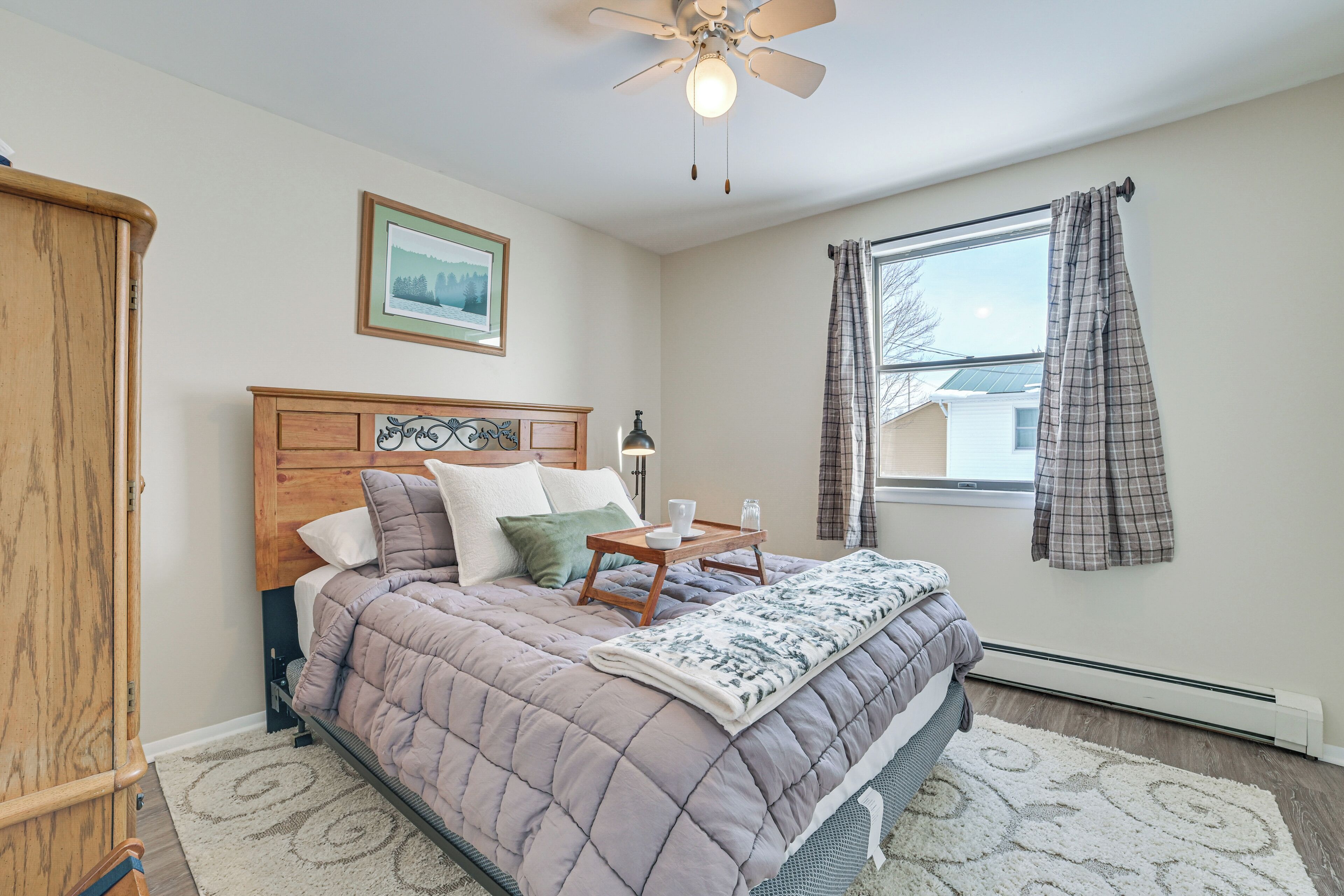 A bedroom with a bed, a ceiling fan, a window with curtains, a heater, and a framed picture on the wall.