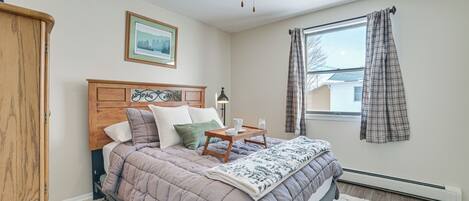 A bedroom with a bed, a ceiling fan, a window with curtains, a heater, and a framed picture on the wall.