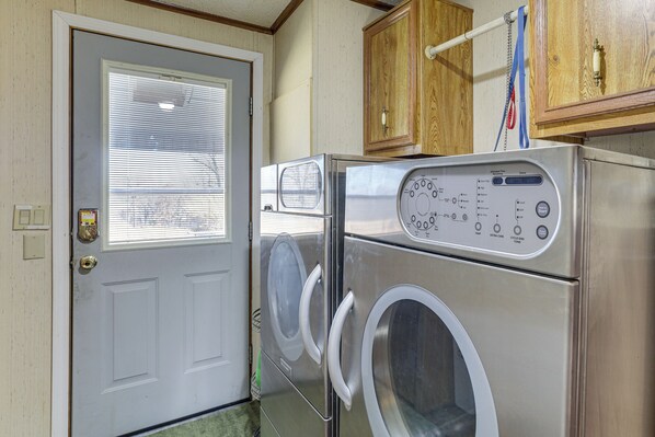 Une petite buanderie équipée d’un lave-linge et d’un sèche-linge à chargement frontal, d’un meuble en bois placé au-dessus du sèche-linge et d’une porte dotée d’une fenêtre.