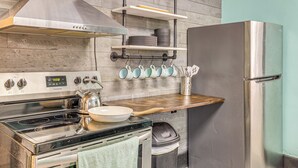 Una cocina con estufa, horno y refrigerador de acero inoxidable, estantes de madera y ollas colgantes.