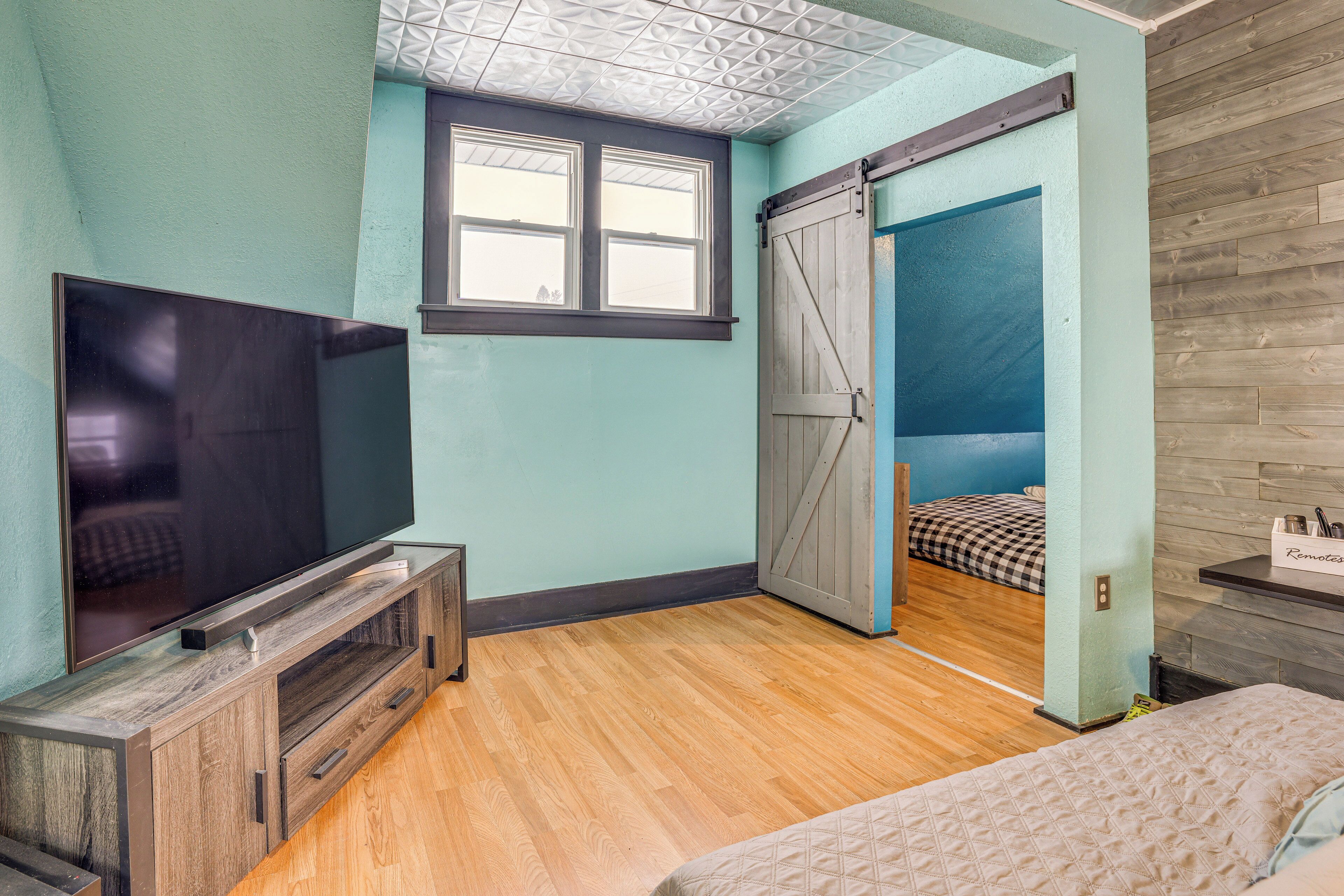 Une chambre dotée d’une télévision, d’un plancher en bois, d’un lit, d’une fenêtre et d’une porte coulissante donnant sur une autre pièce.