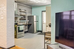 Una cucina moderna con elettrodomestici in acciaio inox, un'ampia televisione a schermo piatto e una parete in mattoni.