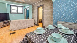 Una habitación con cama, televisor, mesa de comedor con platos y cubiertos, y ventilador de techo.