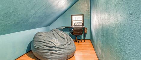 Una habitación pequeña e inclinada con paredes color turquesa, piso de madera, un escritorio con una silla y un sillón de peluche.