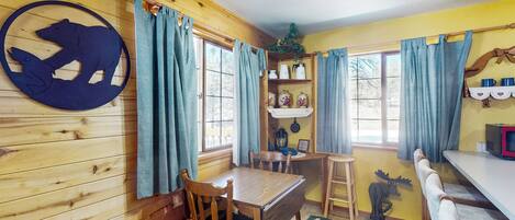 A wooden interior with a dining table, chairs, a bench, and a bear cutout on the wall.