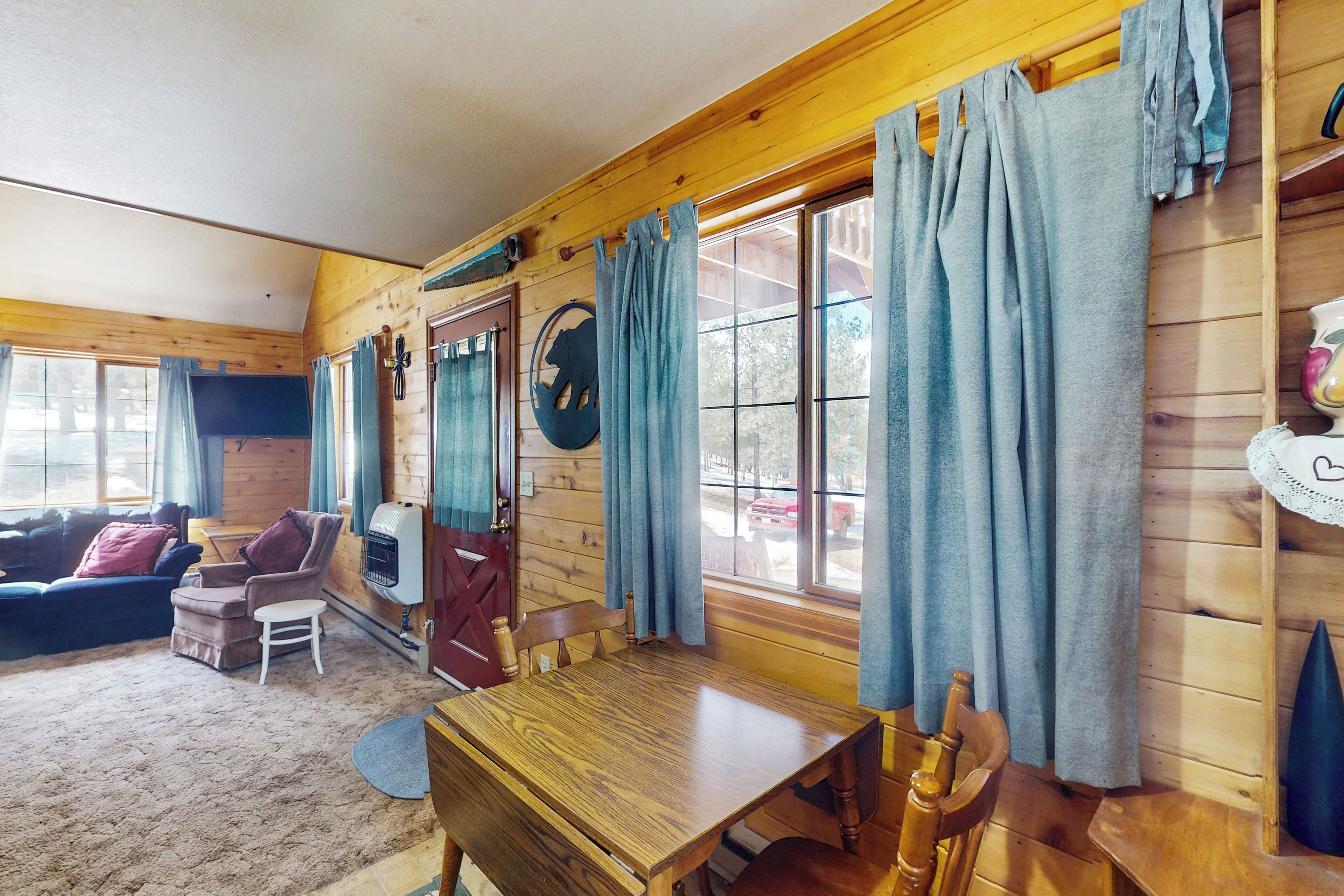 A cozy cabin interior with a wooden dining table, a sofa, and a fireplace.